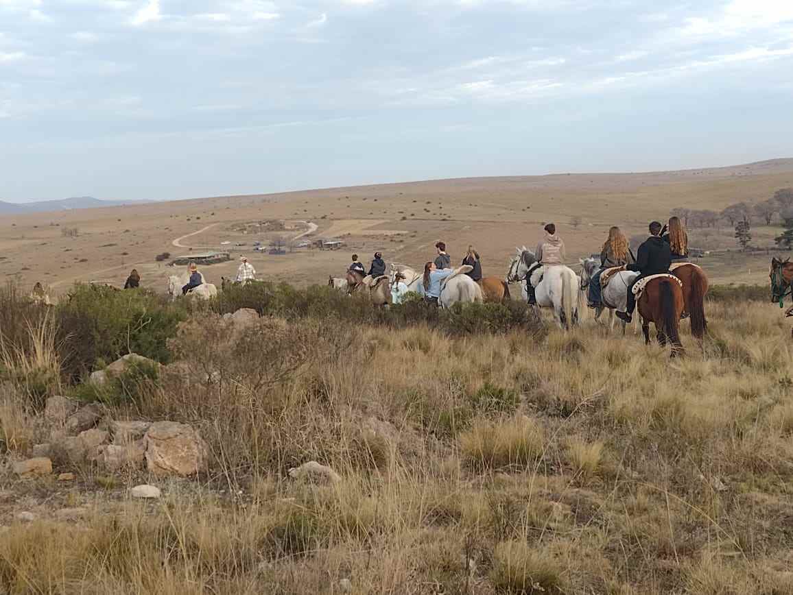Grupo de jinetes sobre una loma, con el campo y las sierras de fondo